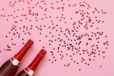 Pembe arka planda konfeti yıldız iki kırmızı Şampanya şişeleri