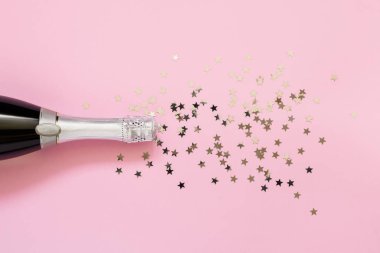 Pembe arka planda konfeti yıldızlı şampanya şişesi. Kopya s