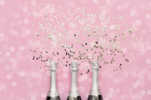 Tres botellas de champán con estrellas de confeti sobre fondo rosa . — Foto de Stock