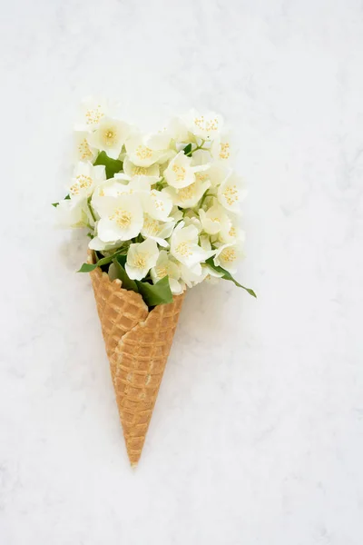 Philadelphus o flores naranjas simuladas en un cono de helado de gofre sobre fondo blanco. Concepto de verano. Copiar espacio, vista superior . — Foto de Stock