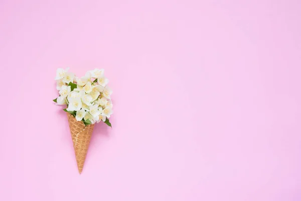 Philadelphus o flores naranjas simuladas en un cono de helado de gofre sobre fondo rosa — Foto de Stock