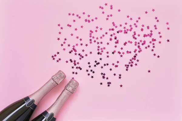 Deux bouteilles de champagne rose avec des étoiles de confettis roses sur fond rose. Couché plat de Noël, anniversaire, bachelorette, nouveau concept de célébration de l'année. Espace de copie, vue du dessus — Photo