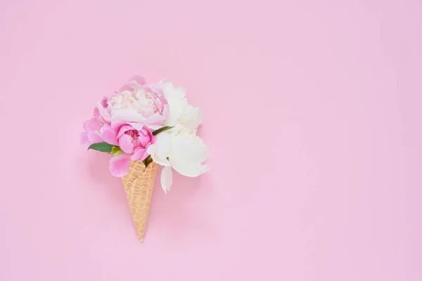 Cono de helado de gofre con flores de peonía sobre fondo rosa. Concepto de verano. Copiar espacio, vista superior — Foto de Stock