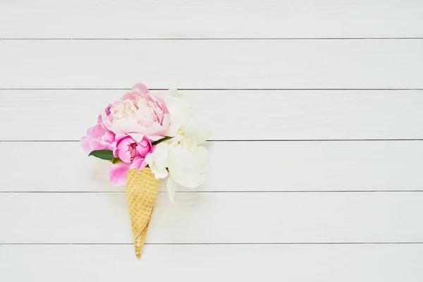 Ramo de flores de peonías en cono de helado de waffle sobre fondo de madera blanca. Concepto de verano. Copiar espacio — Foto de Stock