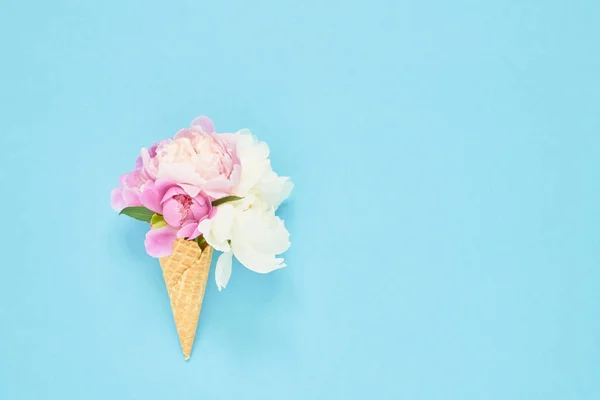 Ramo de flores de peonías en cono de helado de waffle sobre fondo azul claro. Concepto de verano. Copiar espacio, vista superior — Foto de Stock