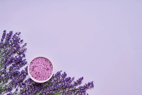 Lavender spa. Lawendy kwiaty i sól do kąpieli w misce na tle liliowy. Kopiuj przestrzeń, widok z góry. Koncepcja Spa. — Zdjęcie stockowe