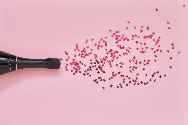 Botella de champán con estrellas de confeti rosa sobre fondo rosa claro. Piso laico de Navidad, aniversario, despedida de soltera, concepto de celebración de Año Nuevo. Copiar espacio, vista superior . — Foto de Stock