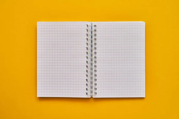空白ページを含む開いているノートブックの上部ビュー。黄色の背景に学校のノート,スパイラルメモ帳 — ストック写真