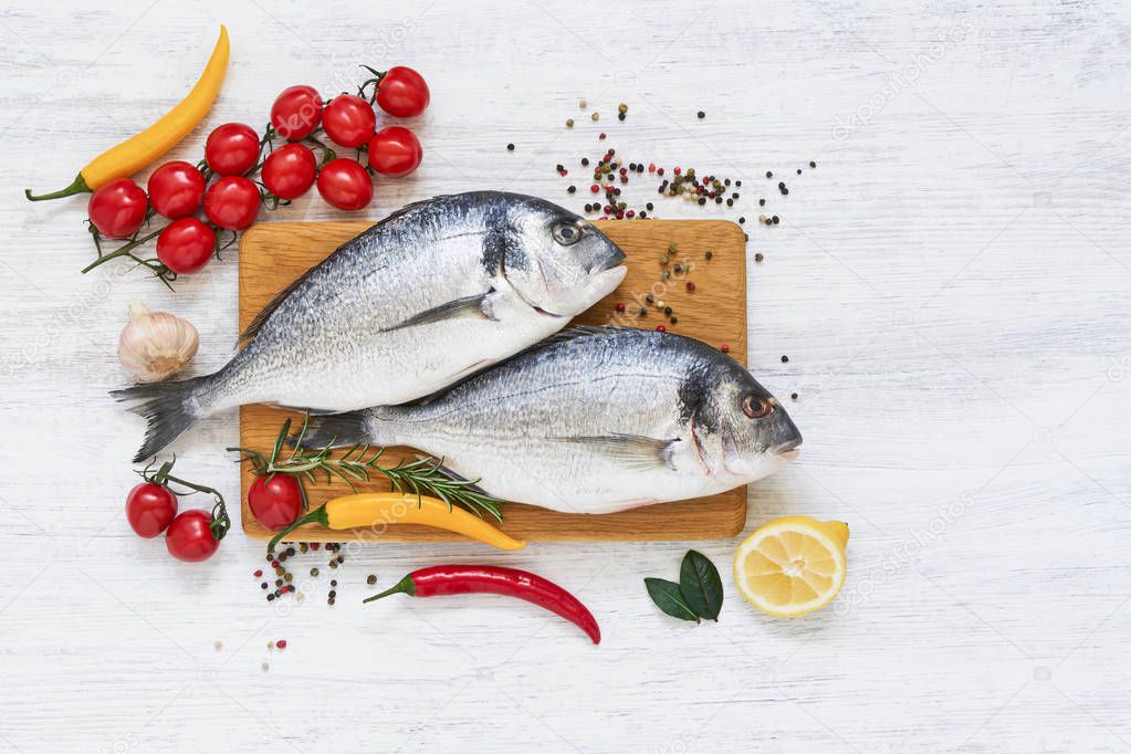 Two raw dorada fish with vegetables on wooden cutting board. Healthy food concept. Top view, copy space. Mediterranean seafood concept.