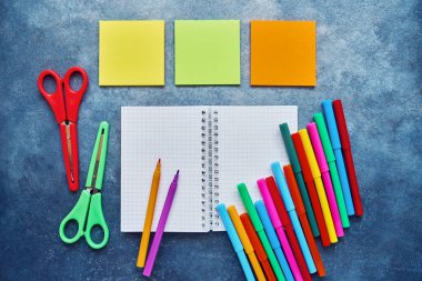 Koyu mavi bir arka plan üzerinde okul konuları. Okul konseptine geri dönelim. Not defteri, çıkartma pedi, renkli makas ve keçeli kalem. Düz döşeme, kopyalama alanı.