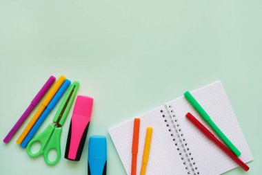 Yeşil arka planda okul konuları. Not defteri, renkli makas ve keçeli kalem. Okul konseptine geri dönelim. Düz döşeme, kopyalama alanı.