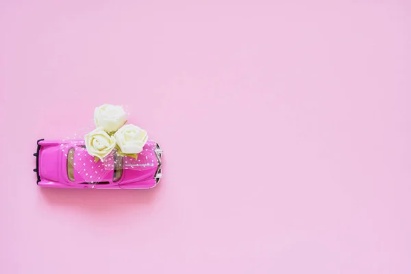 Riga, Letônia - 28 de julho de 2019. Carro de brinquedo retro rosa entregando buquê de flores brancas no fundo rosa. Vista superior, espaço de cópia. Entrega de flores. Cartão de saudação . — Fotografia de Stock
