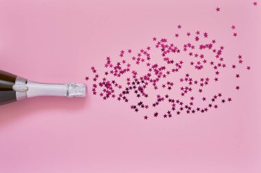 Açık pembe arka planda pembe konfeti yıldızları ile şampanya şişesi. Düz Noel, yıldönümü, Bachelorette, yeni yıl kutlama kavramı yatıyordu. Kopya alanı, üst görünüm.