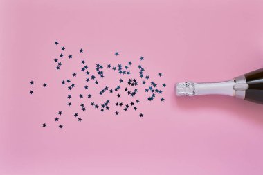 Açık pembe arka plan üzerinde mavi konfeti yıldız şampanya şişesi. Noel, yıldönümü, bekarlığa veda, yeni yıl kutlama konsepti düz yatıyordu. Kopya alanı, üst görünüm.