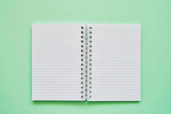 Övre vy av öppen anteckningsbok med tomma sidor, skolans anteckningsbok på en grön bakgrund, spiral anteckningsblock. — Stockfoto