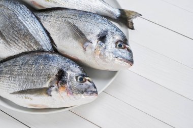 Beyaz masada bir tabak üzerinde dört Taze Kraliyet Dorades. Sağlıklı gıda kavramı. Kopya alanı. Akdeniz deniz ürünleri konsepti.