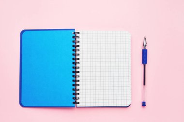 Boş kare sayfaları ve mavi kalemi olan açık bir not defterinin üst görünümü. Pembe arka plan, spiral not defteri. Okul konseptine geri dön.
