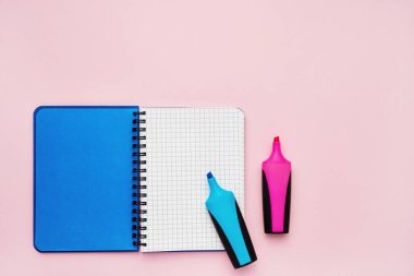 Boş kare sayfaları ve keçeli uçlu kalemleri olan açık bir not defterinin üst görünümü. Pembe arka plan, spiral not defteri. Okul konseptine geri dön