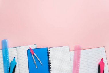 Pastel pembe zeminüzerinde kalem, cetvel ve pusula ile Not Defterleri. Okul konseptine geri dönelim. Sizin için metin, üst görünüm için kopya alanı.