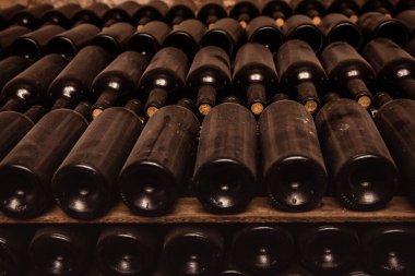 Resting dusty wine bottles stacked on wooden racks in cellar.	