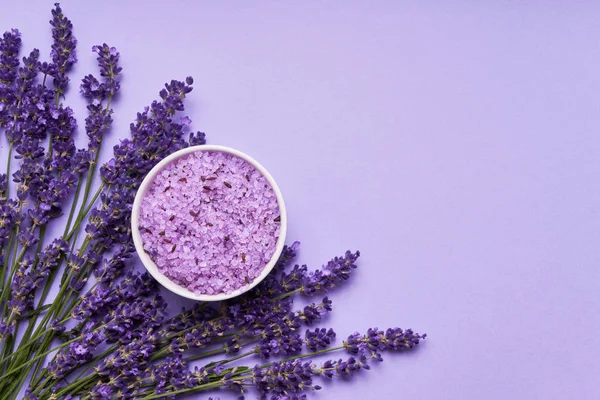 Lavanta Spa. Mor arka planda kase de lavanta çiçekleri ve banyo tuzu. Kopya alanı, üst görünüm. Spa konsepti.
