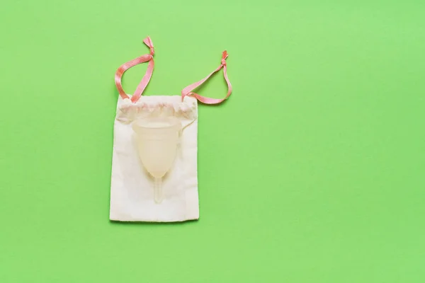 Taza menstrual y bolsa de algodón para guardar sobre fondo azul. Producto alternativo de higiene femenina durante el período. Concepto de salud de las mujeres. Copiar espacio, vista superior . —  Fotos de Stock