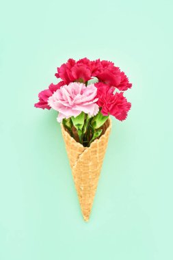 Kırmızı karanfil çiçekleri yeşil arka planda waffle dondurma külahında. Yaz kavramı. Boşluğu kopyala, üst görünüm