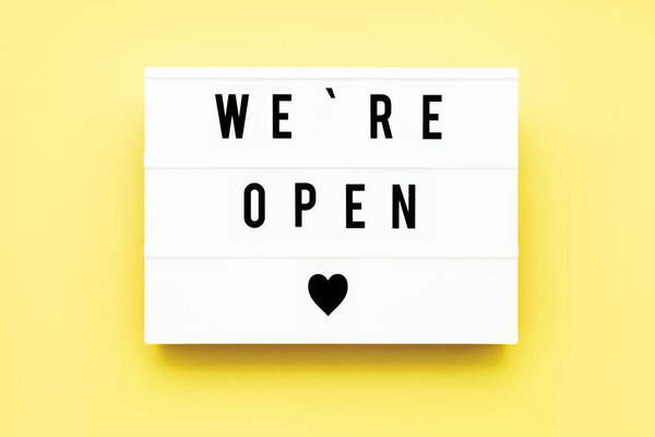 WE'RE OPEN written in light box on yellow background. End of quarantine concept. Copy space, top view