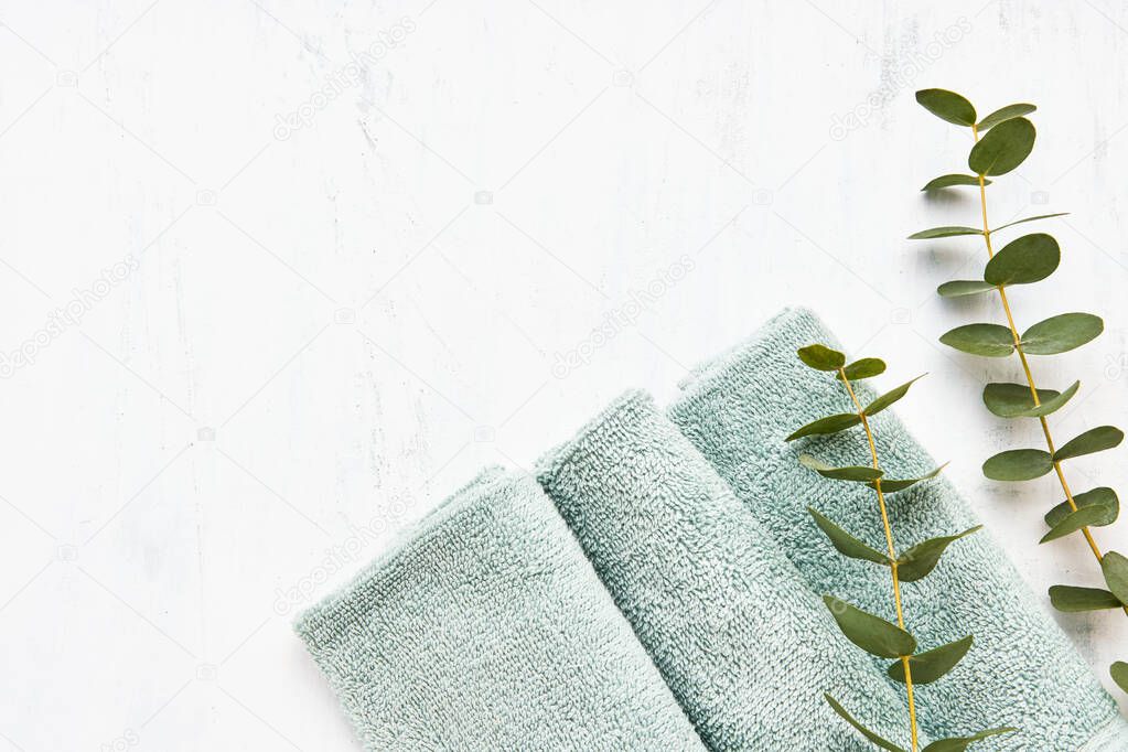 Rolled fluffy towel and green eucalyptus branch on white background. Minimalist scandinavian style. Hygiene, wellness well-being, body care concept. Copy space, flat lay