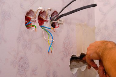 Elektrikçi, konut elektrik tesisatı prizlerini ve anahtarlarını bağlamak için kabloyu söküyor. bir priz aktarılıyor