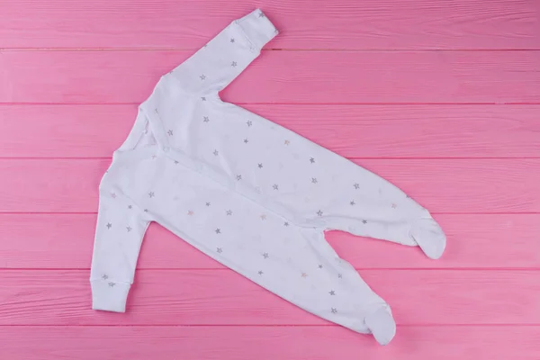 Long-sleeved organic sleep suit for baby. New natural sleep wear with a pattern of stars for infants. Clothes for newborn girl on pink background.