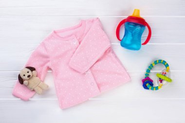 Pembe Bebek kız gömlek ve oyuncaklar. Peluş köpek, şişe ve çıngırak. Beyaz ahşap Resepsiyon arka plan.