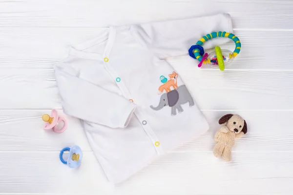 柔らかい赤ちゃんの白いシャツとおもちゃ ガラガラ 木の犬のぬいぐるみナドおしゃぶり — ストック写真