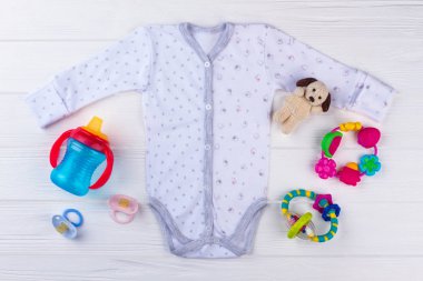 Yeni doğan bebek onesie oyuncaklarla. Beyaz tahta arka plan. Üstten görünüm.