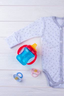 Yeni doğan bebek onesie biberon ve emzik ile. Beyaz tahta arka plan.