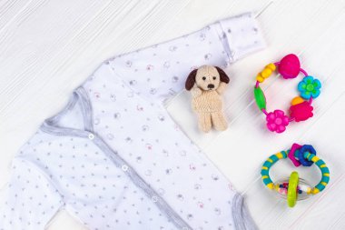 Beyaz bebek onesie ve oyuncaklar. Üstten görünüm. Peluş köpek ve puf sallandı. Beyaz tahta arka plan.