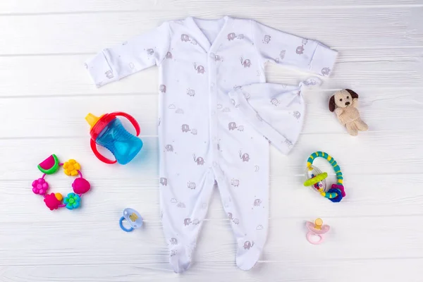 一套婴儿衣服和必需品 白色婴儿睡衣 配有大象 毛绒狗 奶瓶和安抚奶嘴的结帽 图库图片
