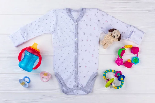 Neugeborenes Baby Onesie Mit Spielzeug Weißer Holzhintergrund Ansicht Von Oben lizenzfreie Stockfotos