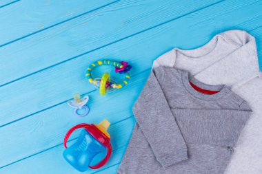 Pamuk bebek creepers ve ihtiyaçlar. Çocuk aksesuarları, çıngırak, emzik ve biberon. Mavi ahşap arka plan.