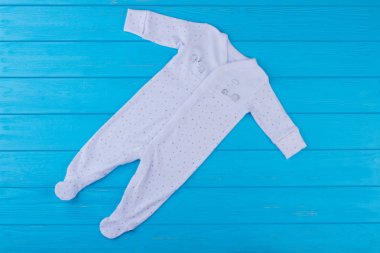 Beyaz yenidoğan onesies ayaklı. Mavi ahşap arka plan.