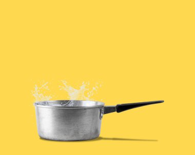 Sarı arka planda izole edilmiş tencerenin kenarında su olan eski bir vintage alüminyum kap.