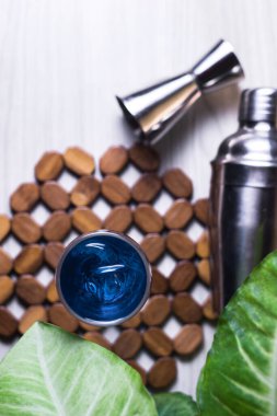 Üst Manzara. Bardakta mavi kokteyl, buz ve kokteyl karıştırıcı ve ahşap masada yeşil yapraklar. Yaz ferahlatıcı kokteyller içecekler. Metin için boşluk ve alanı kopyala