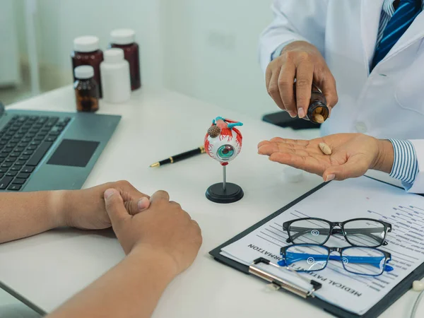 Bir göz doktoru, erkek hastanın zayıf görüşünü göz küresi ve gözlüklerinin bir maketi ile nasıl düzelteceğini tartışıyor..