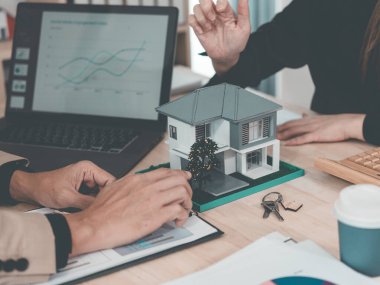 Emlak belgeleri üzerinde çalışan takım elbiseli iki iş adamının yakın çekimi, finansal ayrıntılar, masaya yerleştirilmiş ev modeli, etkili iş toplantısı.