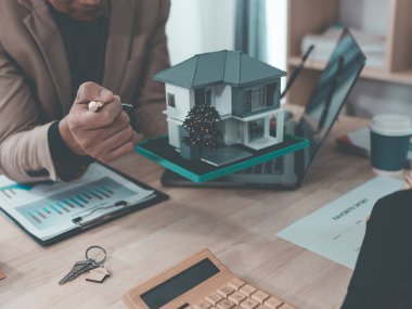 Emlak belgeleri üzerinde çalışan takım elbiseli iki iş adamının yakın çekimi, finansal ayrıntılar, masaya yerleştirilmiş ev modeli, etkili iş toplantısı.