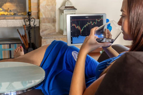 Woman sitting by the fireplace at home investing in the stock exchange - focus on tablet