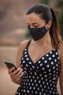 Karantinadan sonra siyah elbiseli ve maskeli bir kadın beyaz noktalarda selfie çekiyor.