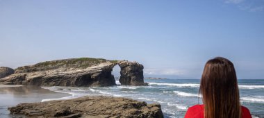 woman watching the beach of the cathedrals in Ribadeo, Galicia, Spain - focus on the rock clipart