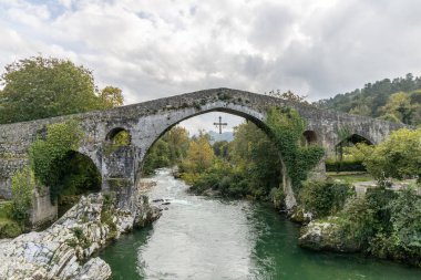 Roman bridge in the city of Cangas de Onis, Spain with the cross of victory hanging from the arch clipart