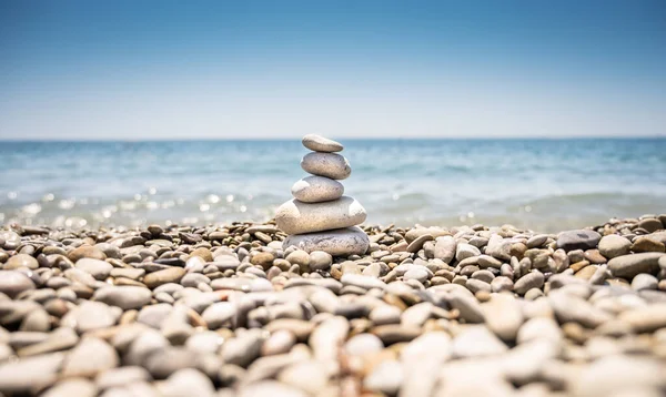 A pyramid of rounded stones of various shapes, sizes and shades. The stones lie one on top of the other from large to small. The building is located on a pebble beach against the backdrop of blue sea